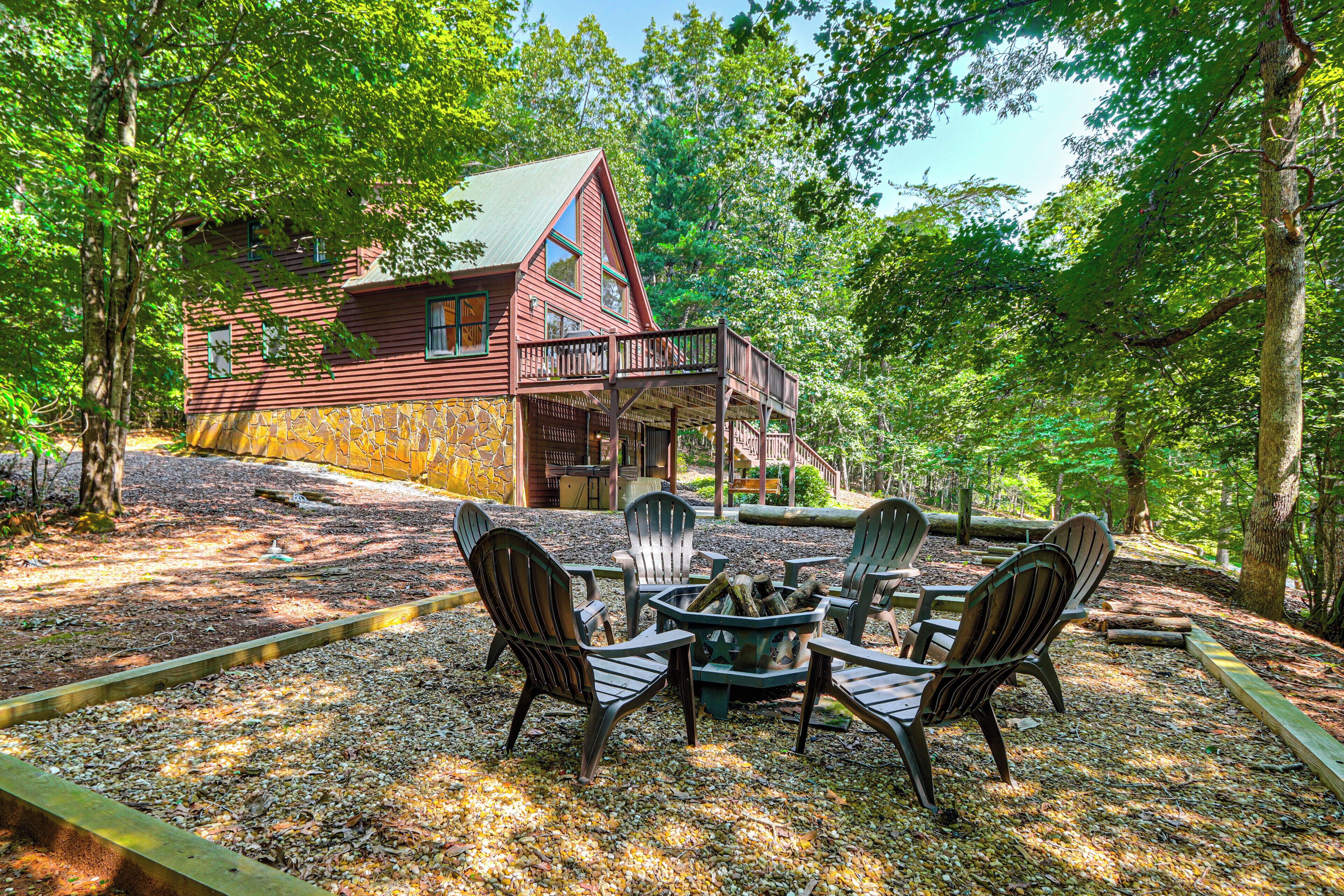 Une cabane dotée d’une terrasse, entourée d’arbres, avec un foyer et des chaises.