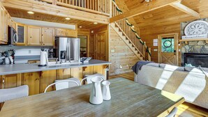 A wooden cabin interior with a kitchen, dining area, and a staircase leading to a loft. - Ellijay Cabin Hot Tub, Mtn Views & Game Room (Ellijay)
