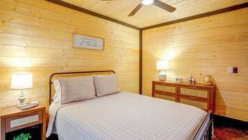A bedroom with a bed, bedside lamps, a ceiling fan, a wooden dresser, and a framed sign on the wall.