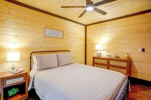 Un dormitorio con cama, lámparas de noche, ventilador de techo, cómoda de madera y un cartel enmarcado en la pared.