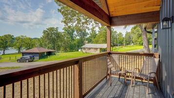 A wooden deck with a railing, overlooking a grassy area with a small cabin and a lake.