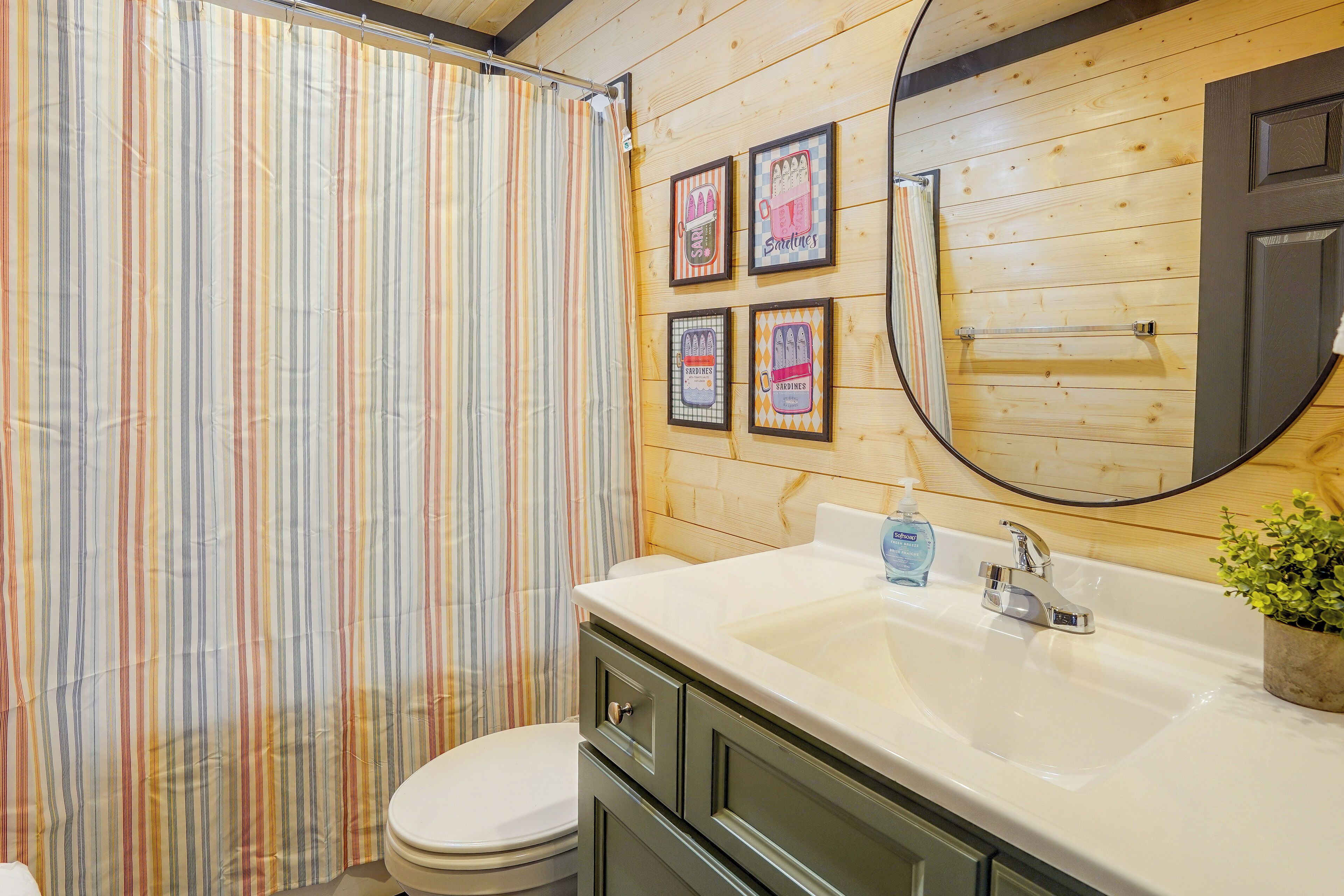 A bathroom with a striped shower curtain, a sink with a soap dispenser, and framed artwork on the wall.