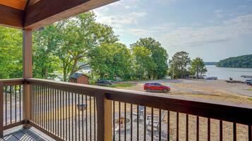 A wooden deck with a view of a lake, boats, and a red car parked on the shore.