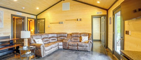 Une pièce chaleureuse avec un grand canapé d’angle, un ventilateur de plafond et un plancher en bois.