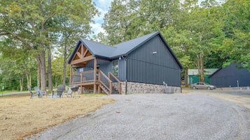 A rustic cabin with a wooden deck and a stone foundation, surrounded by trees.