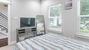 A bedroom with a bed, a TV, a window with blinds, a door, and a staircase. - Walk to Astrodome! Houston Home w/ Balcony (Houston)