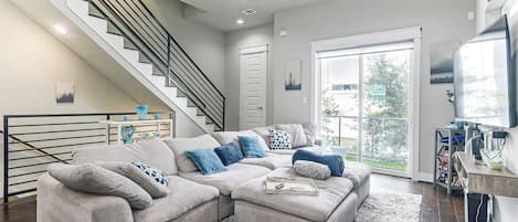 A modern living room with a sectional sofa, a staircase, and a large window.