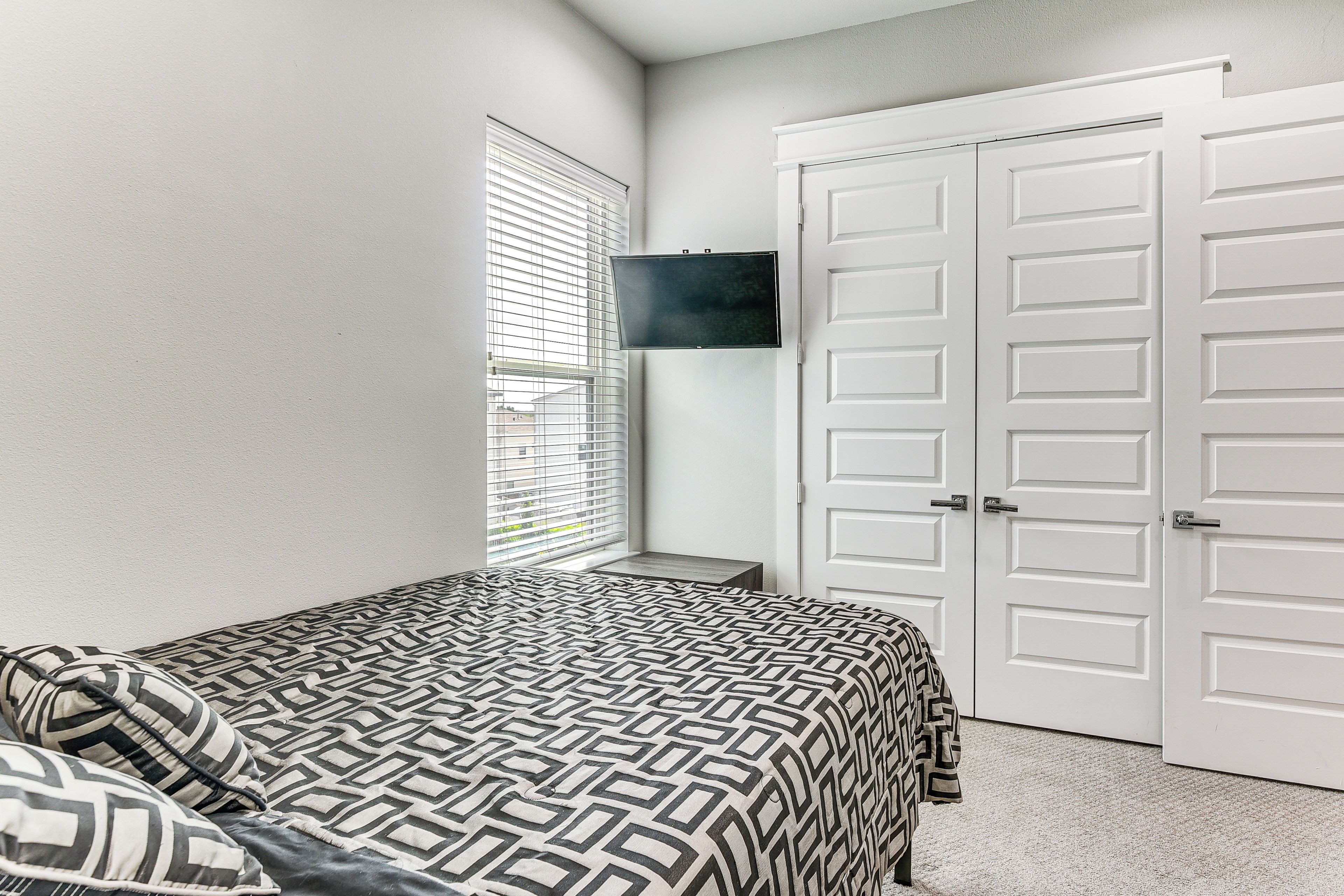 A bedroom with a bed, a TV mounted on the wall, and a closet with double doors.