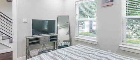 A bedroom with a bed, a TV, a window with blinds, a door, and a staircase.