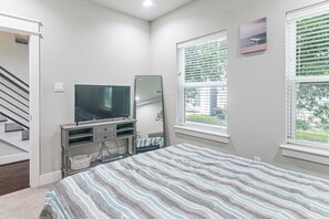 A bedroom with a bed, a TV, a window with blinds, a door, and a staircase. - Walk to Astrodome! Houston Home w/ Balcony (Houston)