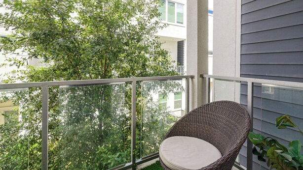 A balcony with a wicker chair, glass railing, and a view of a tree and building. - Walk to Astrodome! Houston Home w/ Balcony (Houston)