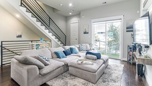 A modern living room with a sectional sofa, a staircase, and a large window. - Walk to Astrodome! Houston Home w/ Balcony (Houston)