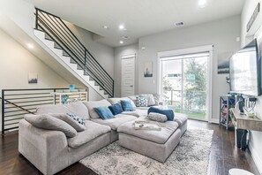 A modern living room with a sectional sofa, a staircase, and a large window. - Walk to Astrodome! Houston Home w/ Balcony (Houston)