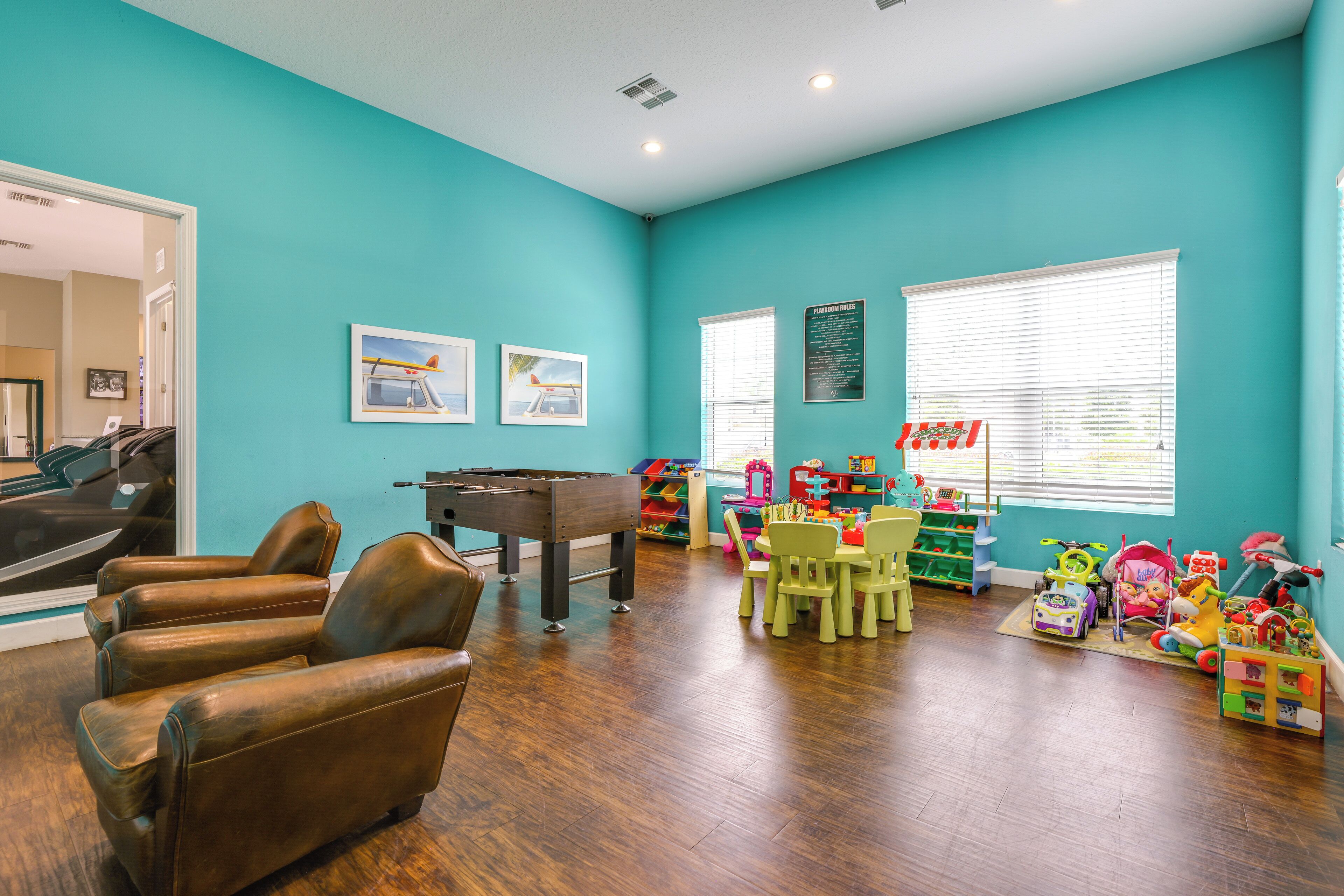 Een kamer in teal met een tafelvoetbalspel, lederen stoelen, een eettafel met stoelen en kinderspeelgoed.
