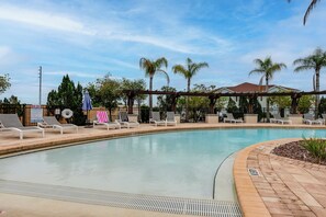 A swimming pool with lounge chairs and umbrellas, surrounded by palm trees and a covered area. - Unwind Poolside, Explore Wdw! Kissimmee Retreat (Kissimmee)