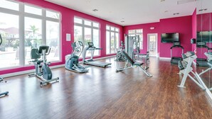 Et fitnesscenter med forskellig træningsudstyr, store vinduer og et fladskærms-tv.