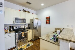 A modern kitchen with stainless steel appliances, white cabinetry, and a granite countertop. - Unwind Poolside, Explore Wdw! Kissimmee Retreat (Kissimmee)