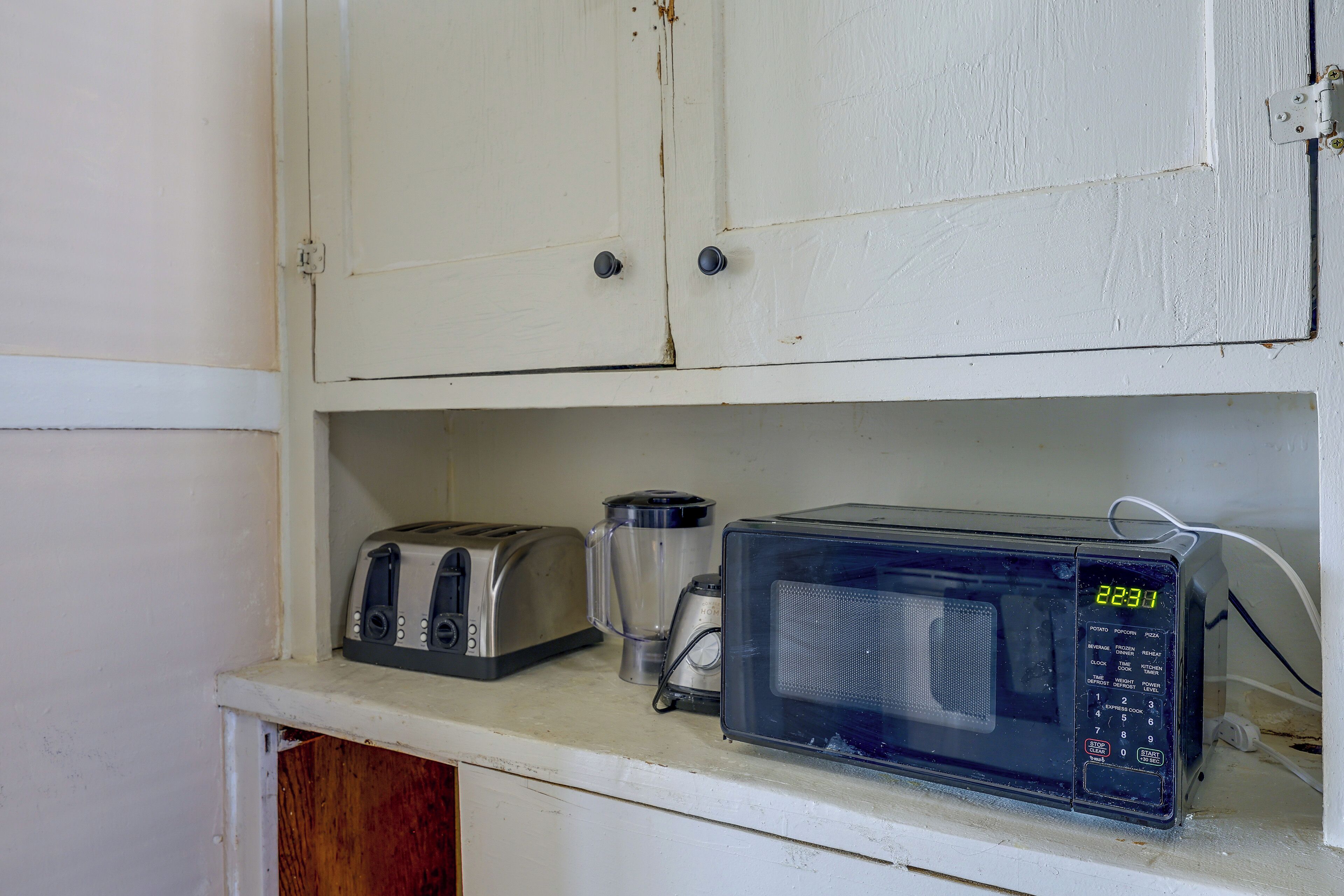 Una kitchenette con tostadora, licuadora y microondas sobre una encimera blanca.