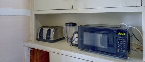 Una kitchenette con tostadora, licuadora y microondas sobre una encimera blanca.