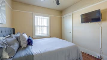 A bedroom with a bed, a ceiling fan, a window, a door, and a television mounted on the wall.