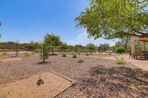 A patio area with a pool, surrounded by gravel and small plants, and a tree providing shade.
