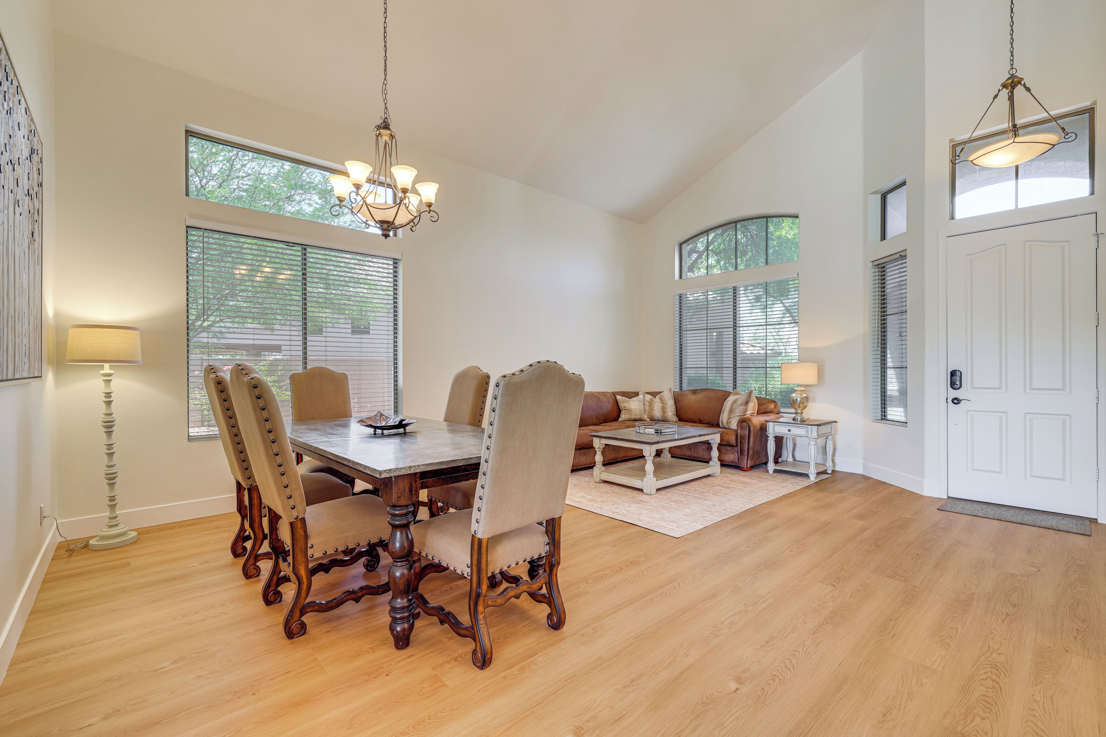 A spacious dining area with a wooden table and chairs, a chandelier, and large windows with blinds.