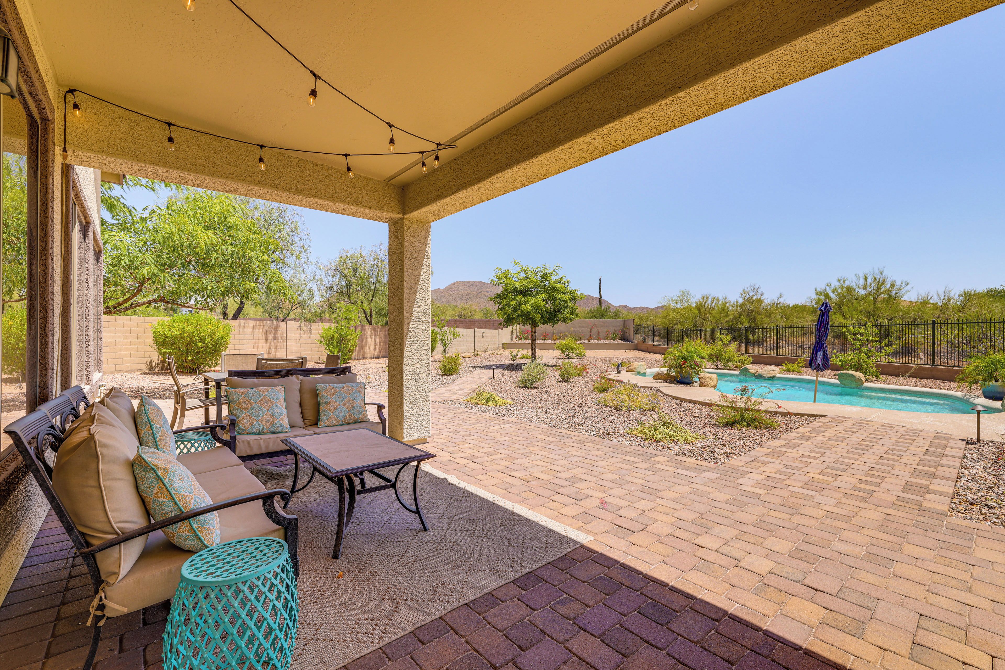 A covered patio area with outdoor furniture, a pool, and a view of the surrounding landscape.