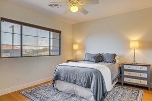 Un dormitorio con cama, dos mesitas de noche, ventilador de techo, ventana y vistas al exterior.