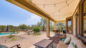 A covered outdoor patio with a pool, seating area, and string lights.