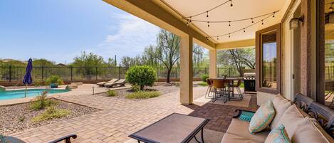 A covered outdoor patio with a pool, seating area, and string lights.