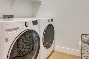 A white LG ThinQ front-loading washing machine with a control panel, a transparent door with a black swirl pattern, and a white wall with a wooden floor. - Fire Pit & Large Yard! Luxury Anthem Escape (Phoenix)