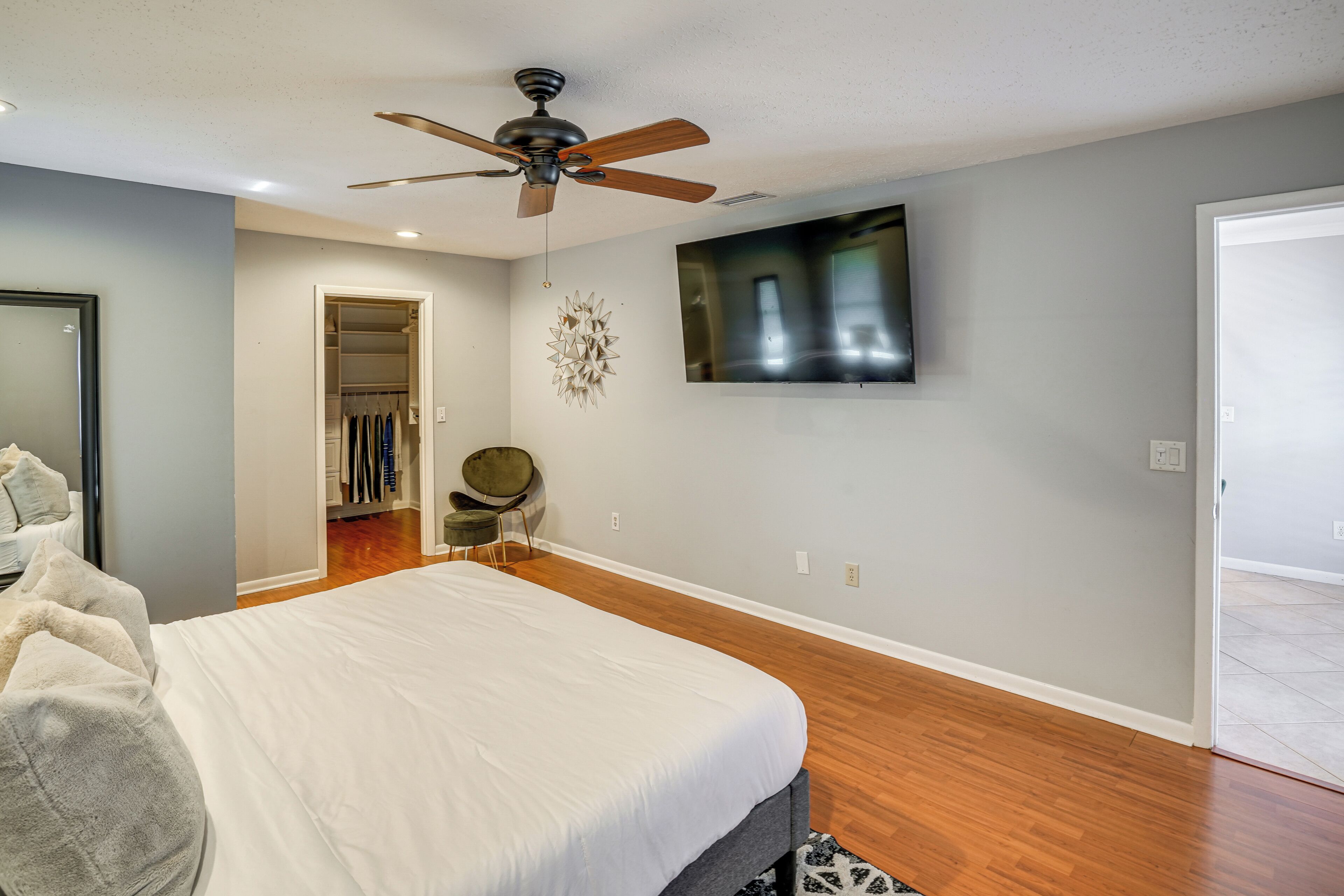 A bedroom with a bed, a ceiling fan, a TV, a closet, and a chair.