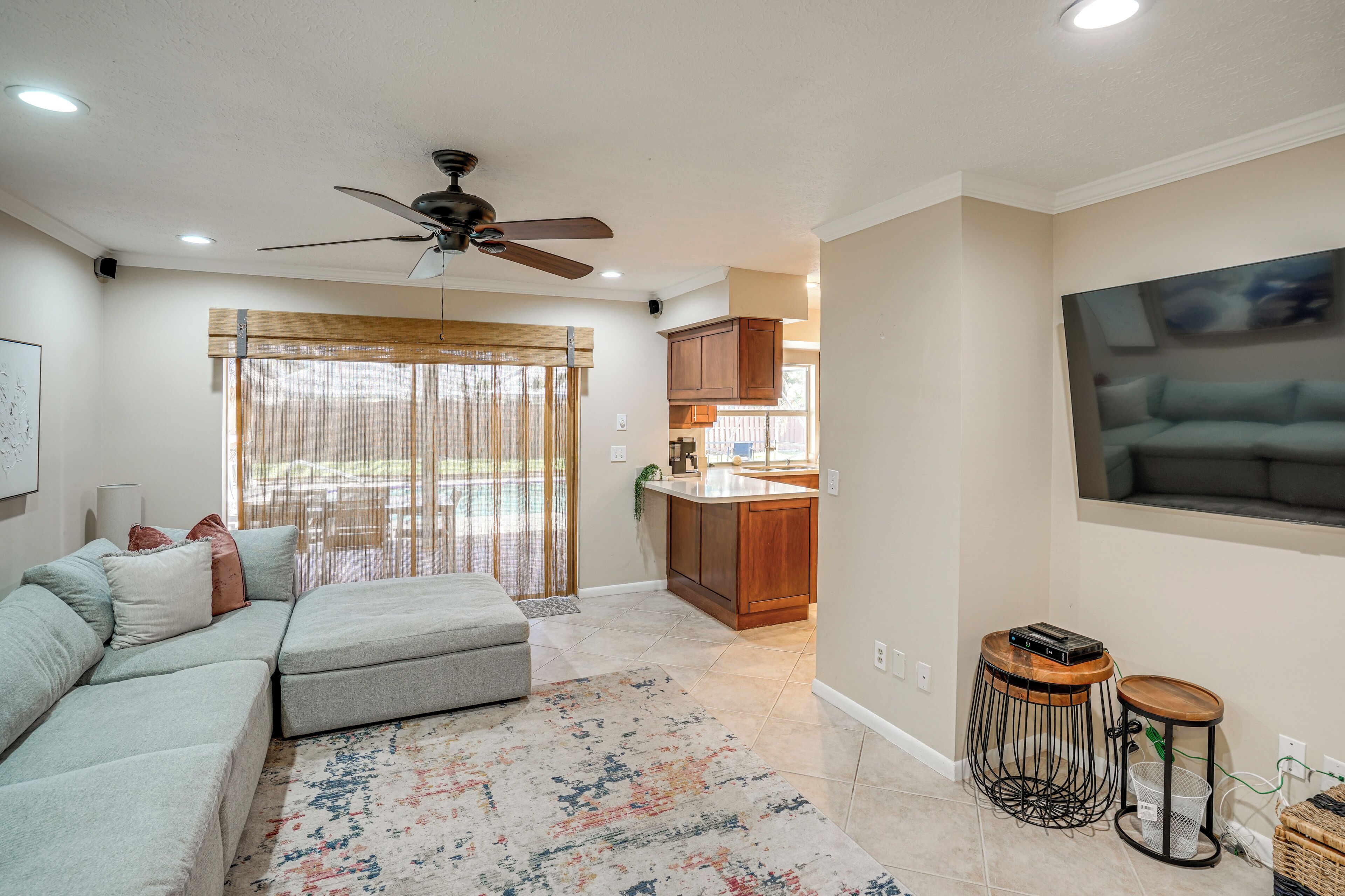 A living room with a sofa, a ceiling fan, and a kitchen area with wooden cabinets.