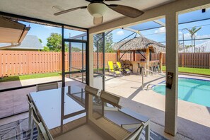 Eine verglaste Terrasse mit Pool, Gartenmöbeln und einem mit Stroh gedeckten Gebäude.