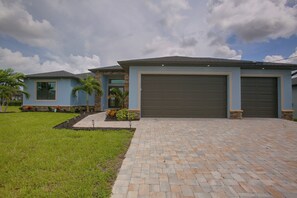 A residential property with a paved driveway, a garage, and a landscaped lawn. - Poolside Paradise in Northwest Cape Coral! (Cape Coral)