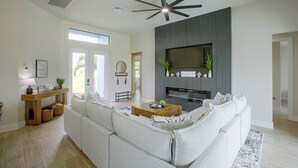 Ein modernes Wohnzimmer mit einer Eckcouch, einem Deckenventilator, einem flachbildschirmfernseher an der Wand und einem Couchtisch aus Holz.