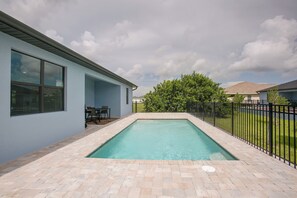 A swimming pool with a brick border, a patio area with a table and chairs, and a security warning sign on a window. - Poolside Paradise in Northwest Cape Coral! (Cape Coral)
