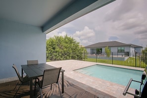 A pool area with a table and chairs, a fenced yard, and a building in the background. - Poolside Paradise in Northwest Cape Coral! (Cape Coral)