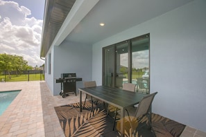 An outdoor patio with a table and chairs, a grill, and a view of a swimming pool. - Poolside Paradise in Northwest Cape Coral! (Cape Coral)