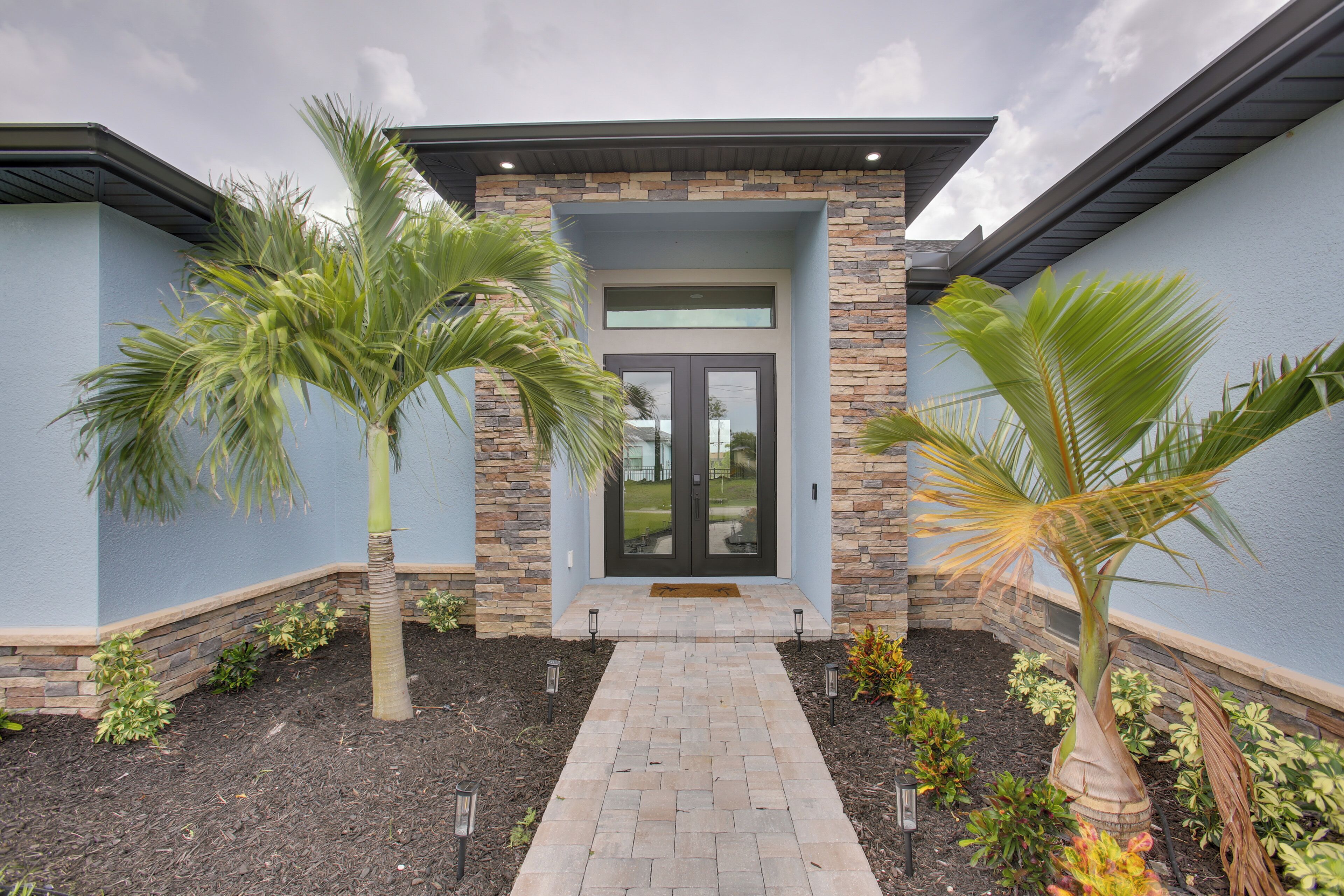A modern building with a stone facade, a central entrance with a glass door, and a paved walkway.
