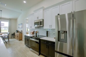 A modern kitchen with stainless steel appliances, wooden cabinets, and a dining area with a view. - Poolside Paradise in Northwest Cape Coral! (Cape Coral)