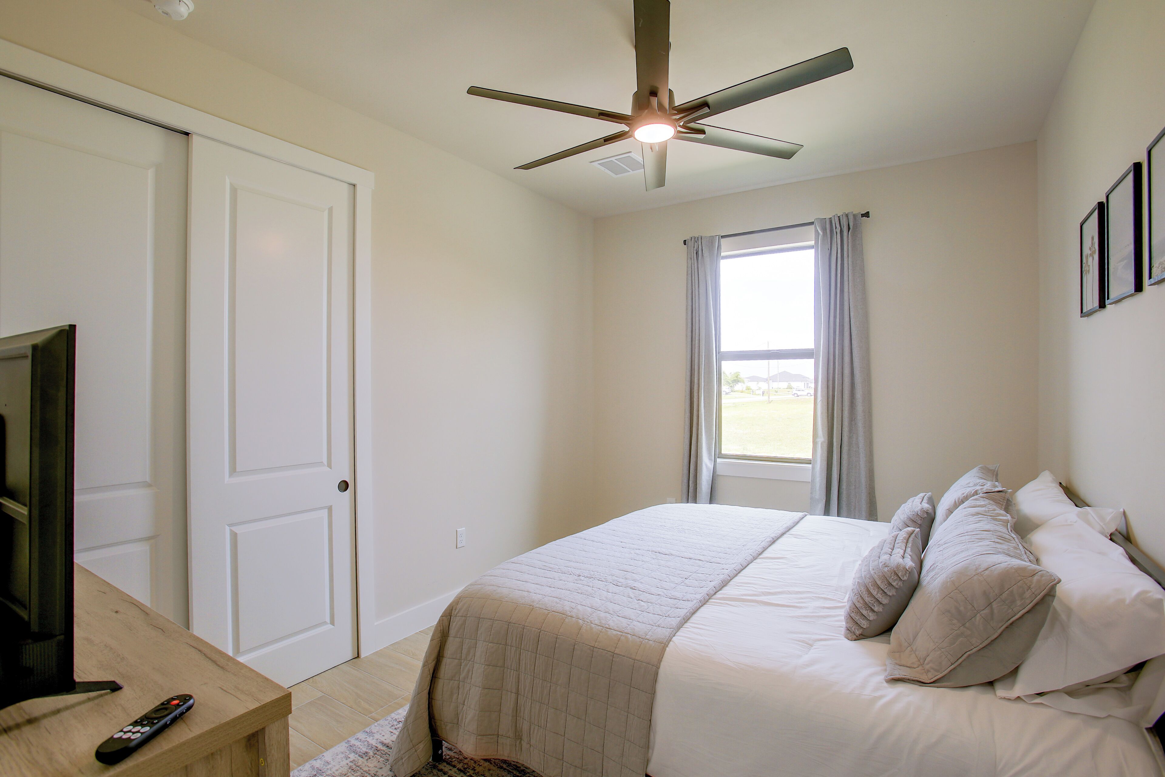 A bedroom with a bed, a ceiling fan, a window with curtains, and a television on a wooden table.