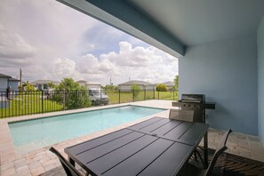 A poolside area with a barbecue grill, a table, and a view of the neighborhood. - Poolside Paradise in Northwest Cape Coral! (Cape Coral)