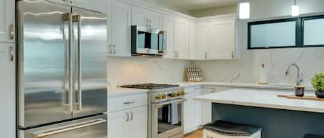 A modern kitchen with stainless steel appliances, white cabinetry, a marble countertop, and a built-in oven.