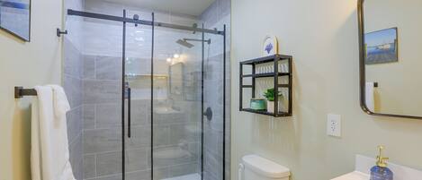 A modern bathroom with a glass-enclosed shower, a toilet, a sink, and a mirror.