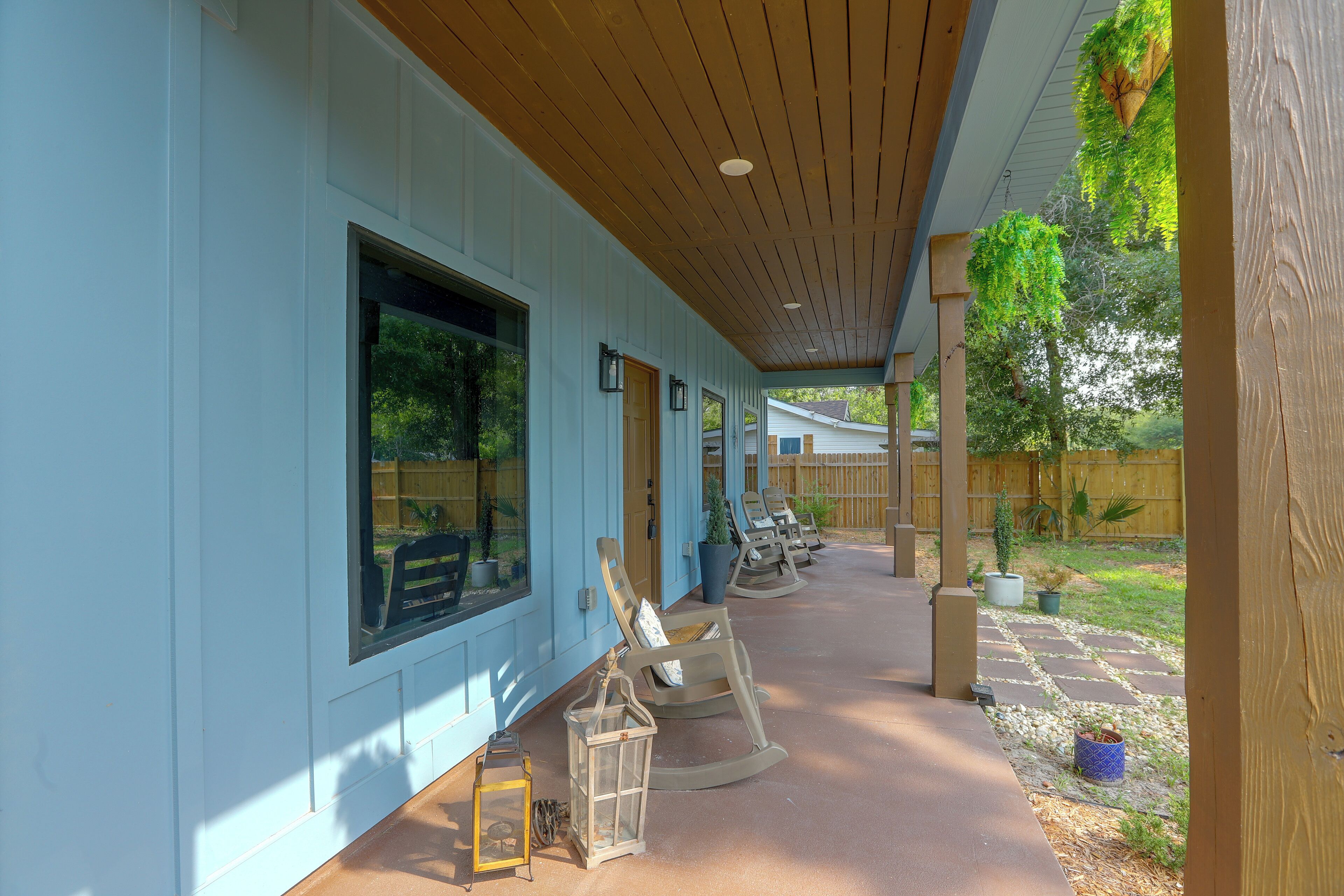 A covered patio area with a wooden ceiling, large windows, and outdoor seating.