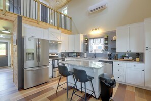 Moderni keittiö, jossa on keskeinen saareke, ruostumattomasta teräksestä valmistetut kodinkoneet ja puinen ylätaso.