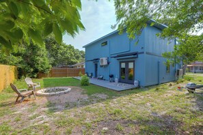 A blue two-story house with a covered patio, a fire pit, and a wooden fence in the background. - Blue Heron - New Modern Home in Carrabelle (Carrabelle)