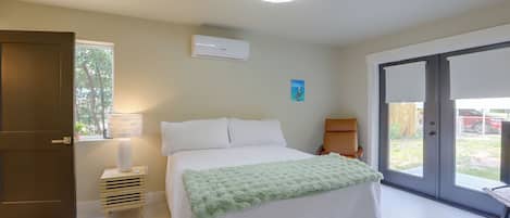 Een slaapkamer met een bed, nachtkastje, lamp, plafondventilator en een raam met uitzicht op de omgeving.