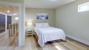 A bedroom with a bed, a nightstand, a lamp, a painting, and a ceiling fan. - Blue Heron - New Modern Home in Carrabelle (Carrabelle)